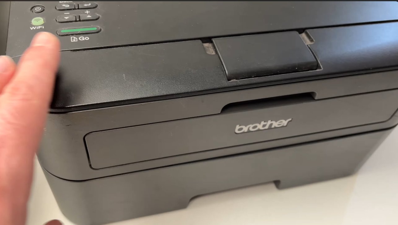 Hand pressing the Go button on a Brother laser printer with the front cover open to reset the drum page counter