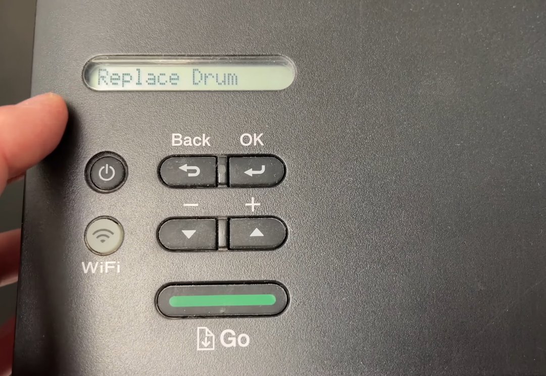 Close-up of Brother printer control panel showing Replace Drum message on LCD display with Go button and OK button visible