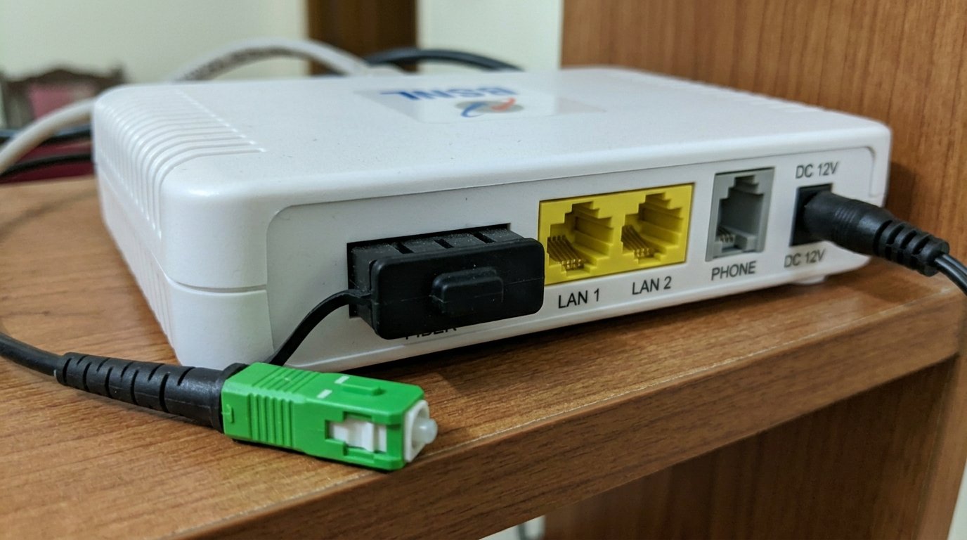 Back panel of BSNL ONT showing fiber connector port labelled FIBER with green SC/APC connector cable, LAN ports and DC power port