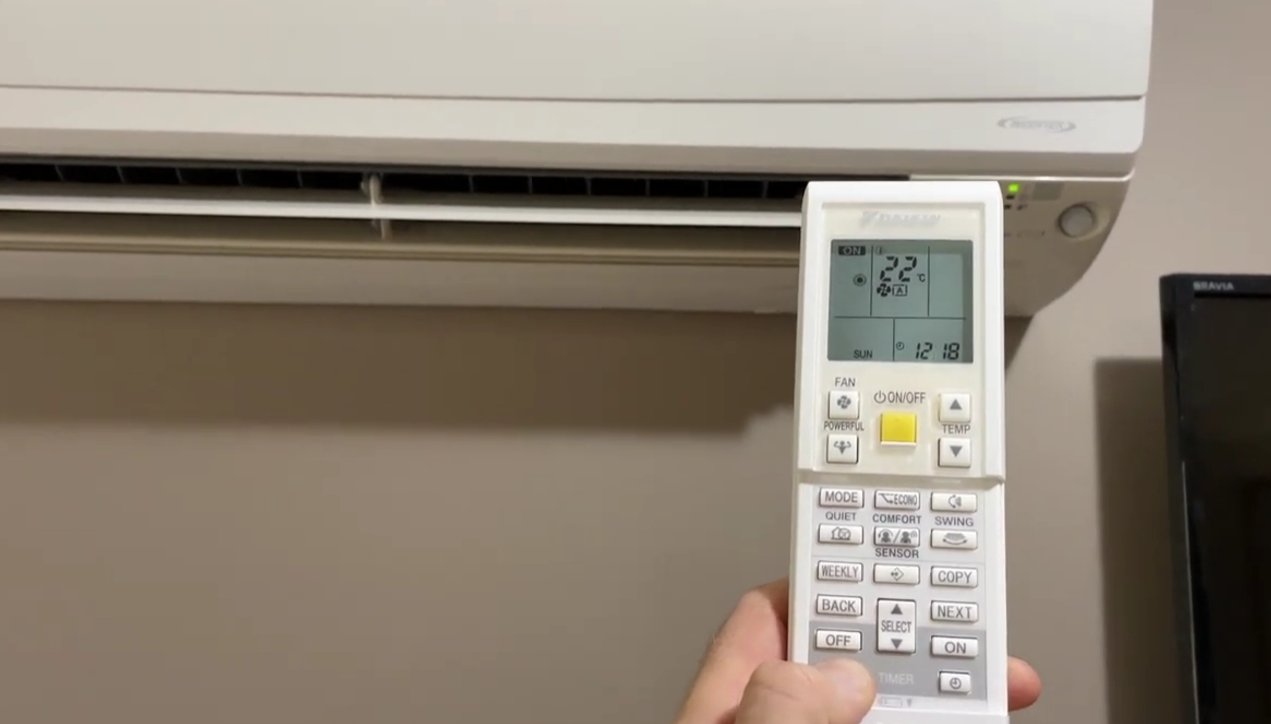 Daikin split AC indoor unit on wall with remote control pointed at it — unit showing error state after E7 fault triggered