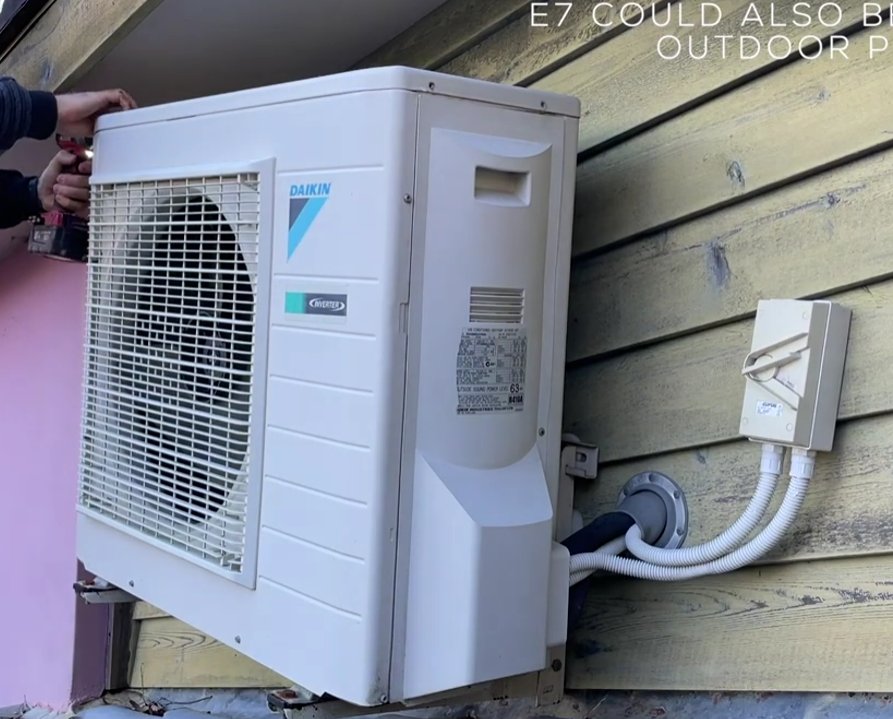 Daikin outdoor unit mounted on wall with hands inspecting the casing — E7 can also indicate outdoor fan issues in some models