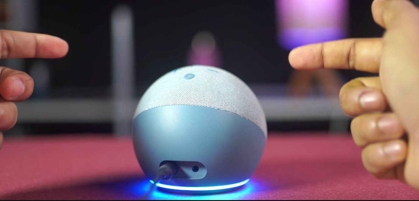 Smartphone showing the Alexa app setup screen next to an Echo Dot with an orange ring in setup mode