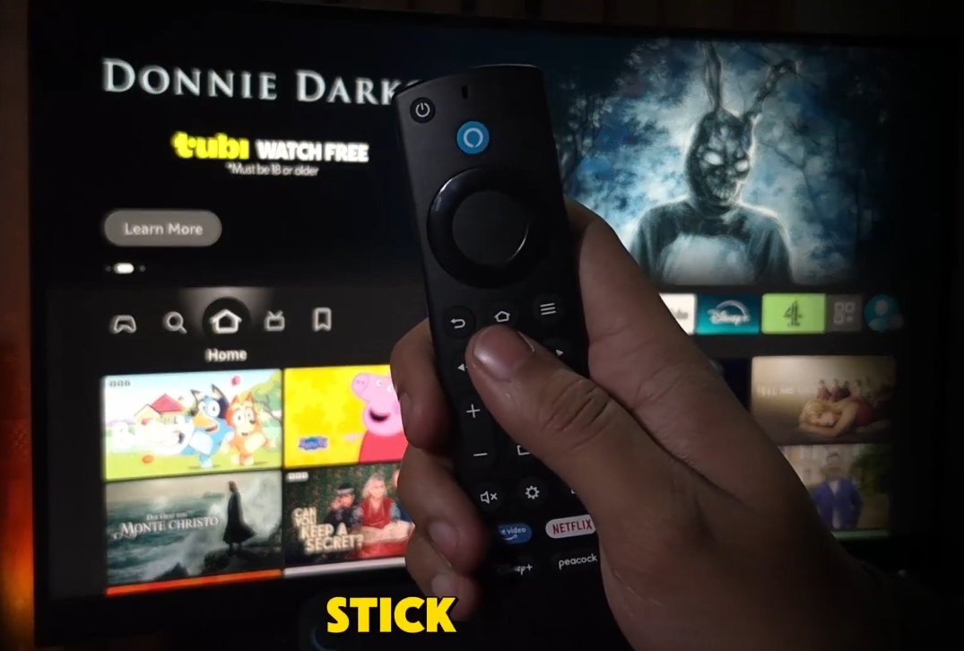 Hand holding Amazon Fire TV Alexa Voice Remote pointing at screen showing the Select button in the centre of navigation ring and other buttons for factory reset combinations