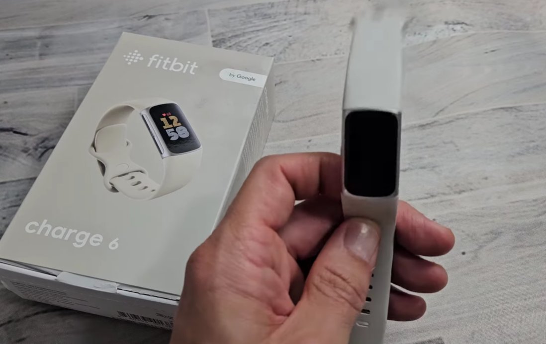 White Fitbit Charge 6 fitness tracker being held in front of its retail box showing a completely black AMOLED display despite being a new device demonstrating the black screen issue on Fitbit Charge series trackers