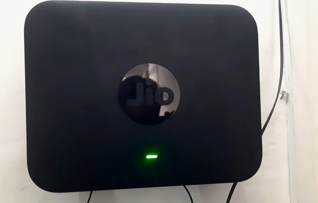 JioFiber ONT device mounted on white wall showing solid green indicator light at the bottom of the device indicating successful optical signal connection and internet working correctly