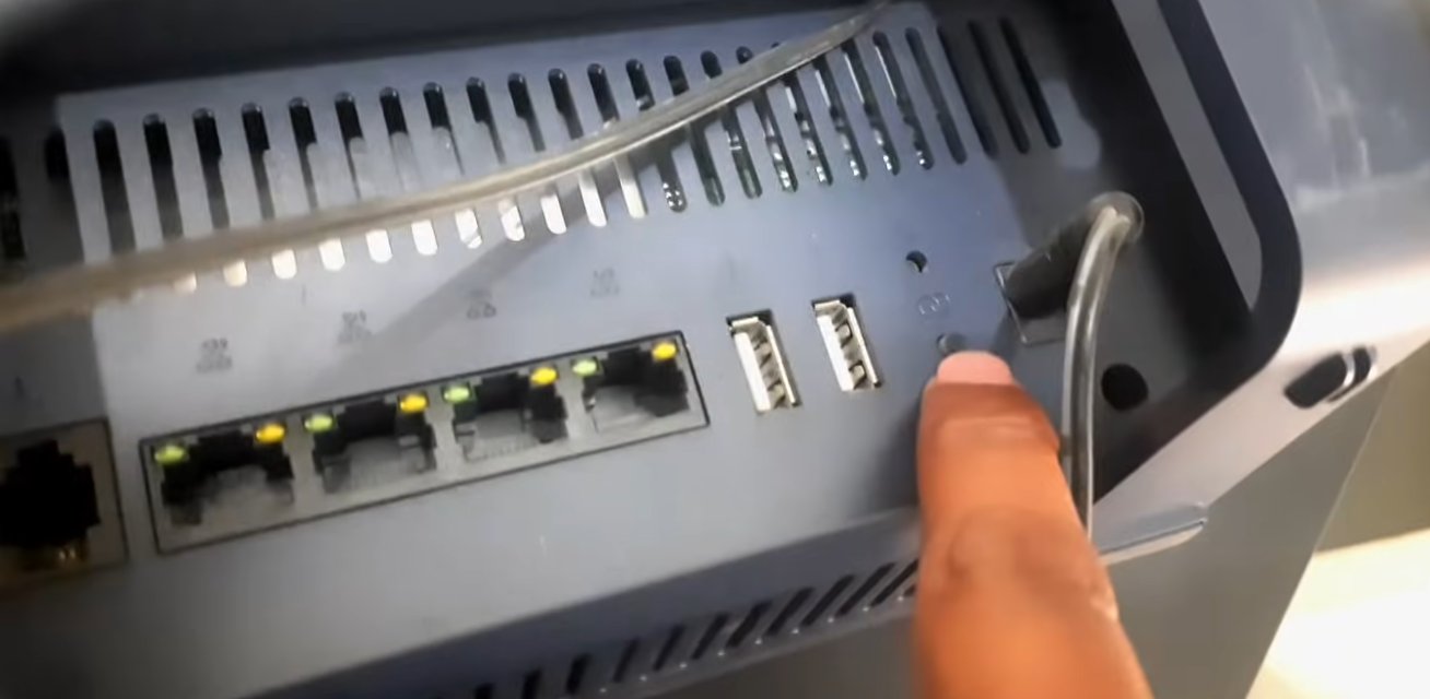JioFiber router back panel showing multiple ethernet LAN ports with green and yellow LEDs plus USB ports with a finger pointing to the reset button location and fibre cable connected at the side