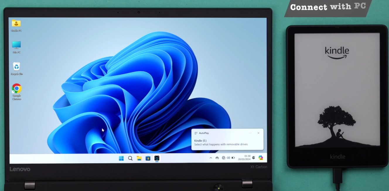 Windows 11 laptop on the left showing the Kindle E drive AutoPlay notification pop-up confirming the Kindle has been recognised as a removable storage device and the Kindle Paperwhite on the right still showing the tree screensaver with USB cable connected