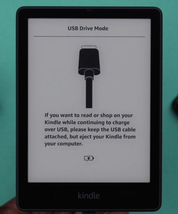 Kindle Paperwhite showing USB Drive Mode screen with cable icon and instructions saying if you want to read or shop while continuing to charge over USB please keep the USB cable attached but eject your Kindle from your computer confirming successful USB connection and partial recovery