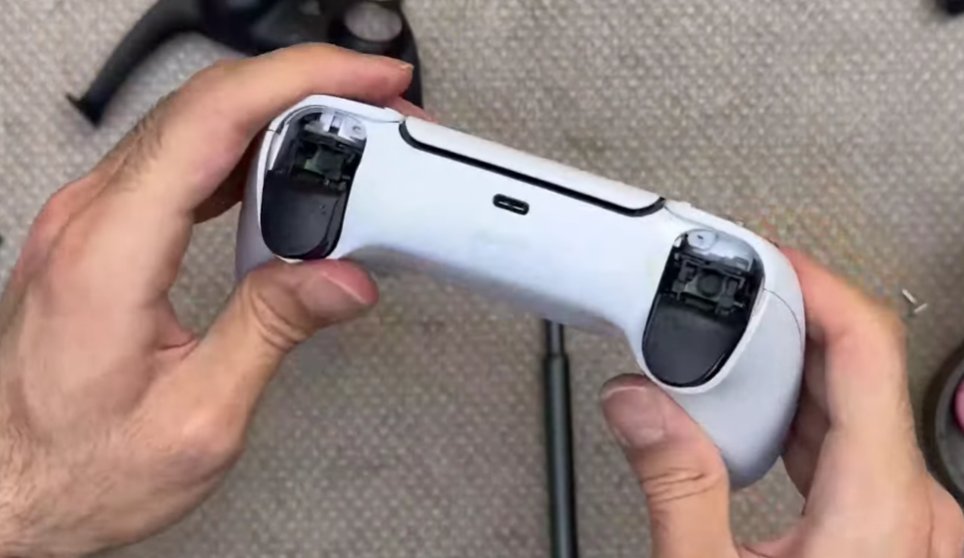PS5 DualSense controller held showing the back and bottom edge with the USB-C charging port visible in the centre and the L2 R2 trigger buttons the small reset button hole is located near the L2 trigger