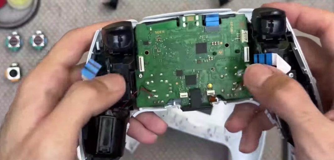 PS5 DualSense controller opened with both halves separated showing the green main PCB motherboard with analogue stick modules visible at top left and top right of the board and replacement Hall effect stick modules laid out beside the opened controller