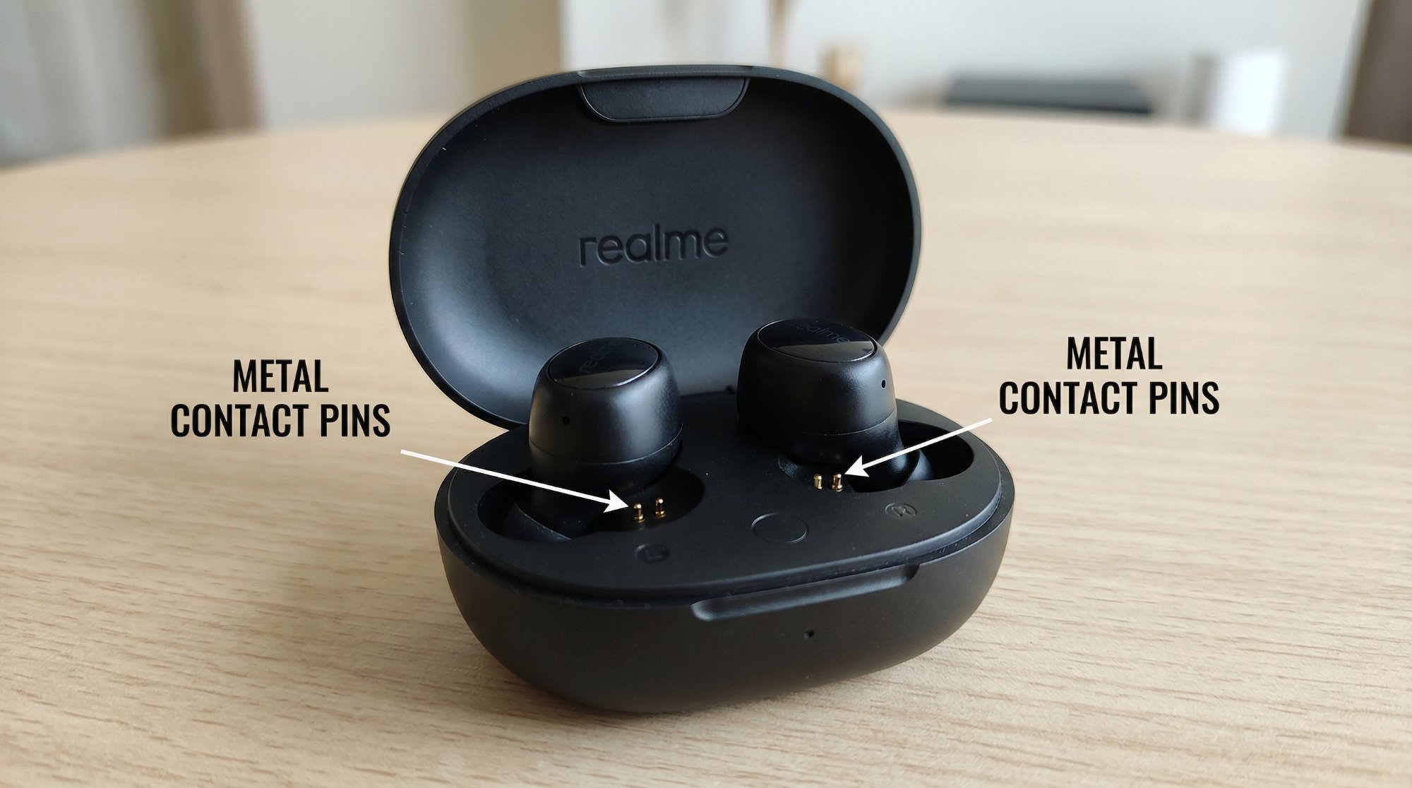 Realme buds charging case open showing gold metal contact pins inside the bud wells with labels pointing to each pin