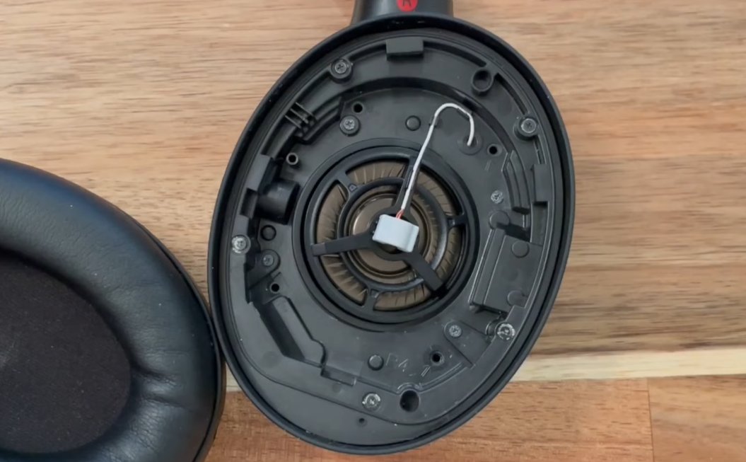 Sony WH-1000XM4 earcup fully disassembled showing the large circular 40mm driver unit in the centre of the housing with earcup removed on the left and ANC microphone wiring visible around the driver frame
