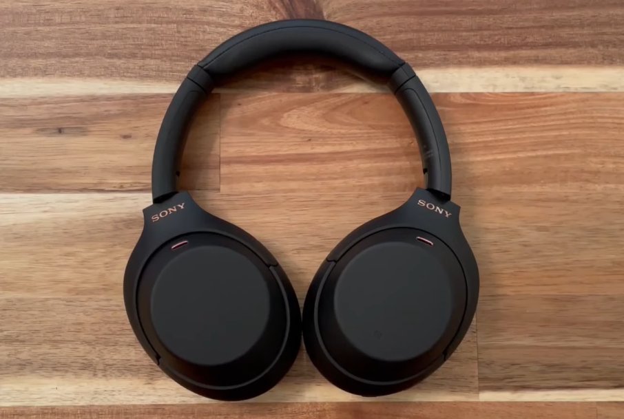 Sony WH-1000XM4 headphones lying flat on a wooden surface front view showing both earcups with SONY branding and the red indicator light positions on each cup