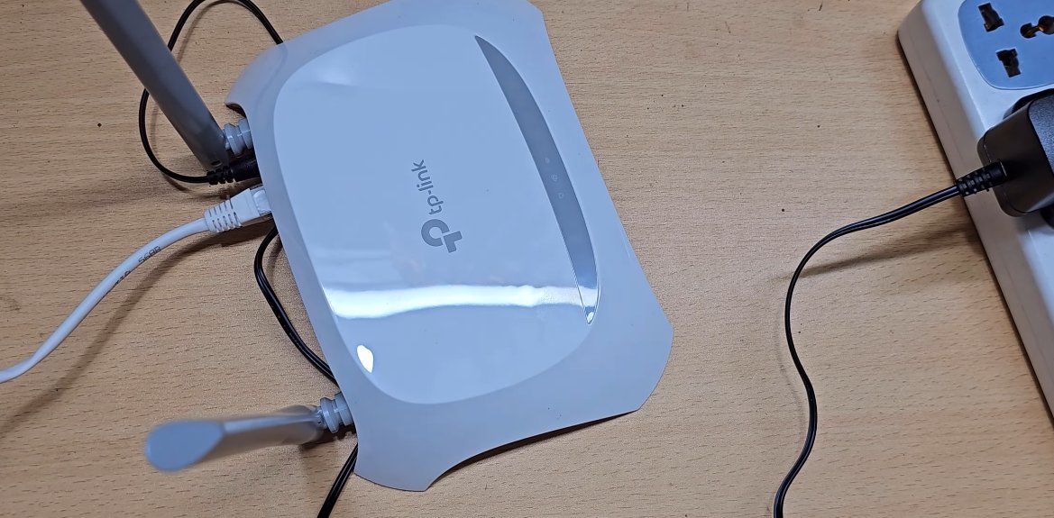 TP-Link router on a desk with its power cable connected to a power strip, ready for a power cycle to fix the orange light